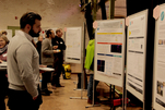 Blick in die Veranstaltungshalle. Mehrere Personen schauen sich die ausgehängten Poster an.