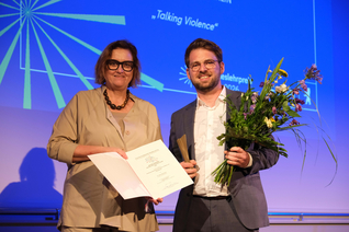 Ina Czyborra und Jannis Julien Grimm posieren auf der Bühne mit Urkunde und Blumenstrauß