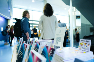 Infostand mit Flyern in einem Foyer mit vielen Menschen