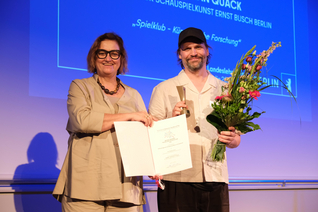 Ina Czyborra und Sebastian Quack posieren auf der Bühne mit Urkunde und Blumenstrauß