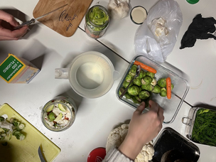 fotografiert wurde ein Tisch von oben, darauf schneiden Menschen Gemüse wie Blumenkohl und Möhren zu