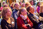 Blick ins Publikum: Vorn im Bild, drei Menschen mit Brille, die ihren Blick nach rechts neigen.