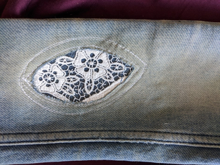 Foto einer Jeanshose, bei der das Loch am Knie mit einem Stück Spitze geflickt wurde