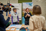 Zwei Personen stehen vor einem Poster und einem Roll-up. Darauf zu lesen: „Zukunft findet Stadt“. Von hinten zu sehen sind Prof. Dr. Yasmin Olteanu und eine Person mit einer Filmkamera.