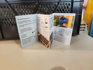 Flyer Biodiversität Das Foto zeigt einen selbsterarbeiteten Flyer, der aufgefaltet auf einem Tisch steht. Es gibt Informationen zu Biodiversität, dem Bau von Minibeeten und Insektentränken. Der Text ist nur bedingt lesbar.