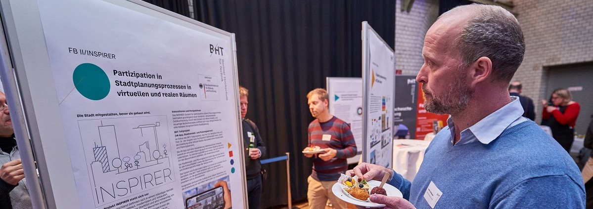 Eine Person schaut auf ein Poster. Darauf steht: Partizipation in Stadtplanungsprozessen in virtuellen und realen Räumen“